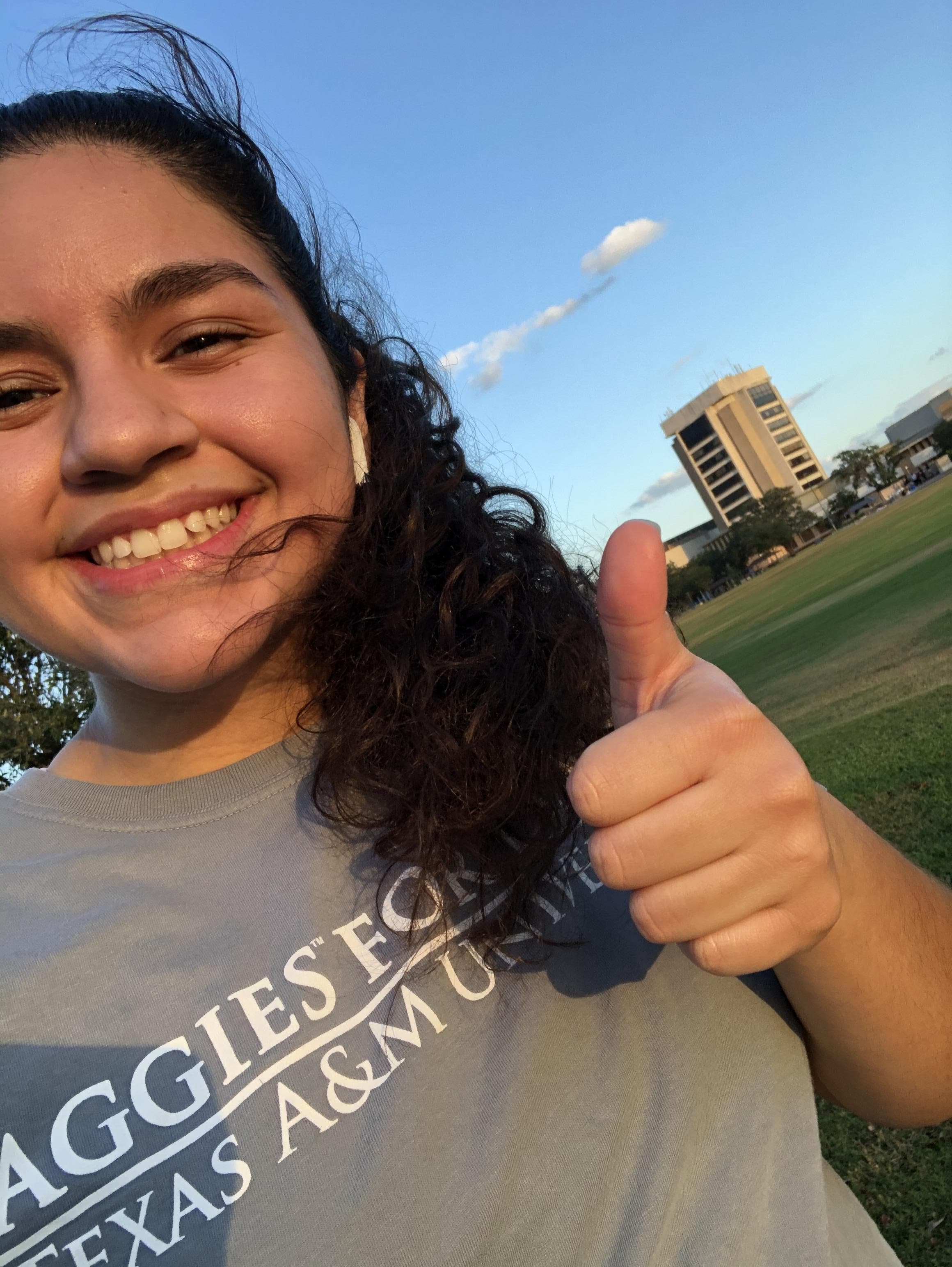 AFL member's selfie wearing organization t-shirt and giving thumbs up, with campus building visible in background