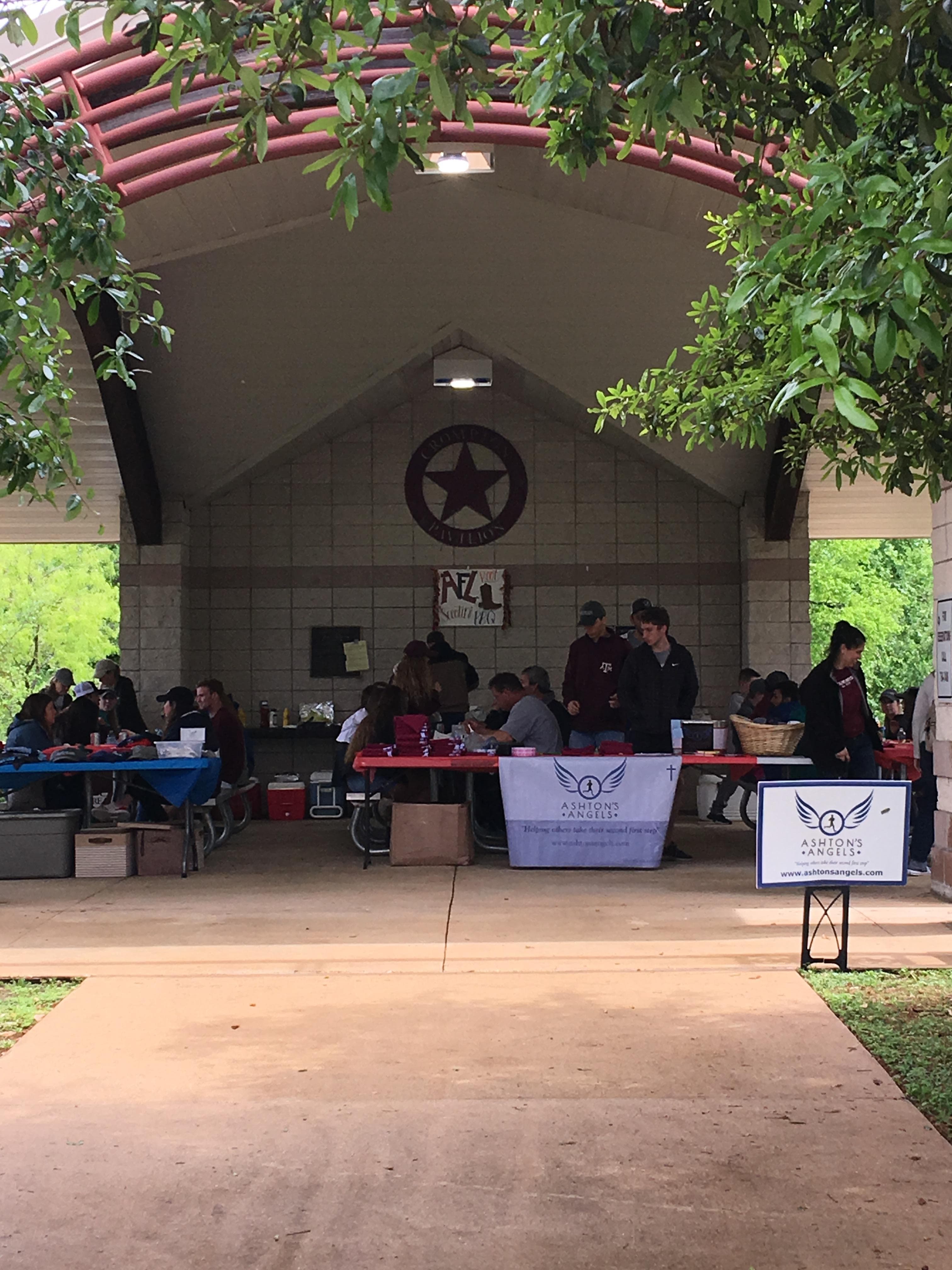 Event registration setup with Aggies for Limbs banners and check-in tables at a covered pavilion with a Texas star emblem